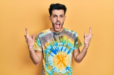 Latin asıllı genç adam, gündelik kıyafetler giyip çılgın bir ifadeyle bağırıyor ve elleri havada rock sembolü yapıyor. Müzik yıldızı. ağır kavram. 