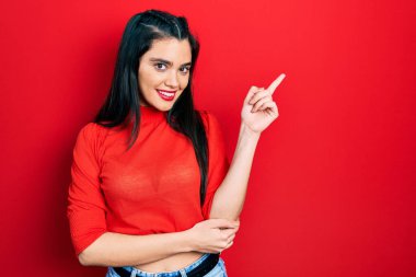 Gündelik kıyafetler giyen genç İspanyol kız gülümseyerek mutlu bir şekilde elini ve parmağını kenarda gezdiriyor. 