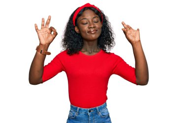 Güzel Afrikalı genç kadın rahat kıyafetler giyiyor ve gözleri kapalı gülümsüyor parmaklarıyla meditasyon hareketi yapıyor. yoga konsepti. 