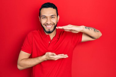 Sakallı, sıradan kırmızı tişörtlü, elleri büyük ve büyük boy işareti gösteren İspanyol bir adam. Kameraya bakıp gülümsüyor. ölçüm kavramı. 