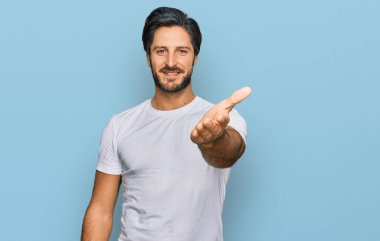 Latin asıllı genç bir adam, günlük beyaz tişörtler giyip dostça bir şekilde el sıkışarak selamlıyor ve hoş geldin diyor. başarılı iş. 