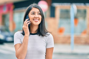Genç İspanyol kadın gülümsüyor. Şehirdeki akıllı telefondan konuşuyor..