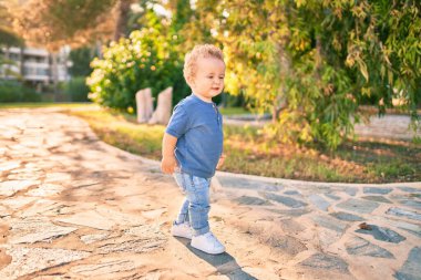 Sevimli ve mutlu küçük çocuk güneşli bir günde parkta eğleniyor. Güzel sarı saçlı erkek çocuk dışarıda oynuyor.