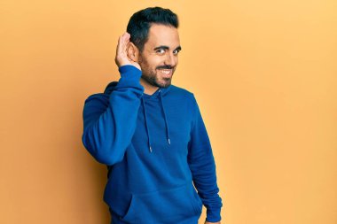 Gündelik kıyafetler giyen, ağzı kulaklarında gülümseyen genç İspanyol bir adam dedikoduları ve dedikoduları dinliyor. Sağırlık kavramı. 