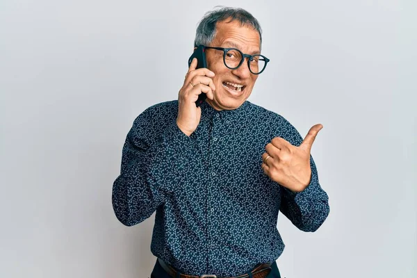 印度中年男子 一边用智能手机交谈 一边把大拇指指向一边 高兴地张开嘴 — 图库照片