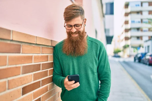 Young irish man with redhead beard smiling happy and using smartphone at the city.