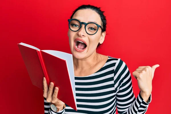 Young Caucasian Woman Wearing Glasses Covering Mouth Book Pointing Thumb — 스톡 사진