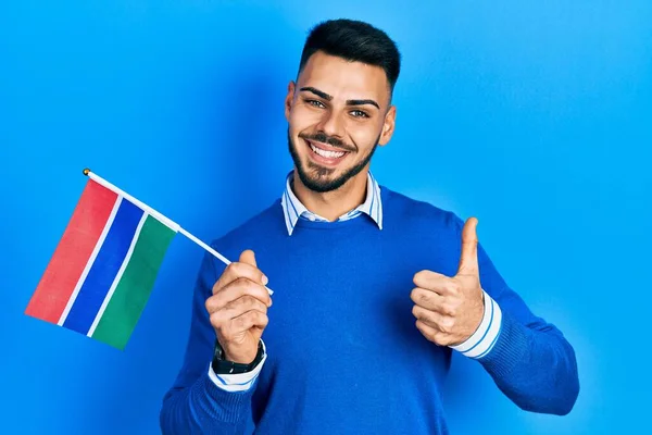 Ung Latinamerikansk Man Med Skägg Håller Gambia Flagga Ler Glad — Stockfoto