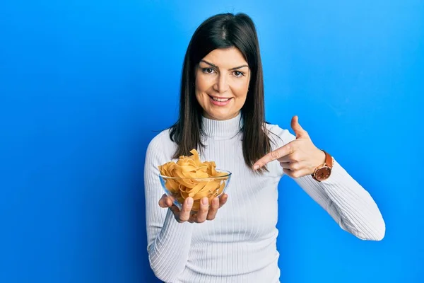 Jovem Hispânica Segurando Tigela Macarrão Não Cozido Sorrindo Feliz Apontando — Fotografia de Stock