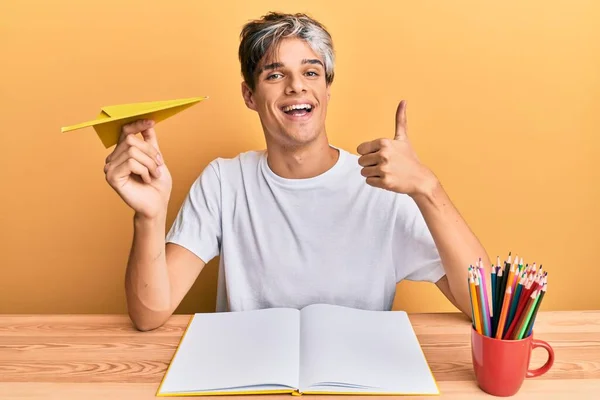 Młody Latynos Studiujący Trzymający Papierowy Samolot Siedzący Stole Uśmiechnięty Szczęśliwy — Zdjęcie stockowe