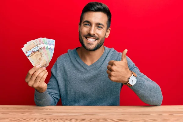 Hombre Hispano Guapo Sosteniendo Dólares Canadienses Sonriendo Feliz Positivo Pulgar —  Fotos de Stock