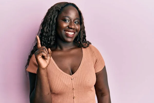 アフリカの若い女性が幸せな顔で指を指してアイデアや質問と笑顔カジュアルな服を着て ナンバーワン — ストック写真