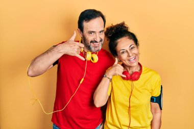Orta yaşlı bir çift İspanyol kadın ve erkek spor giyer ve kol bandı takar telefon hareketlerini telefonda konuşur gibi yaparlar. iletişim kavramları. 