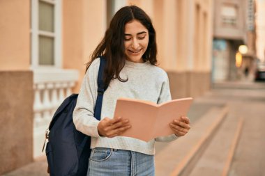 Genç ortadoğu öğrencisi kız şehirde mutlu bir şekilde kitap okuyor..