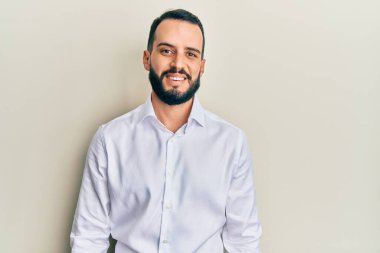 Sakallı genç bir adam beyaz iş gömleği giyiyor ve yüzünde mutlu ve havalı bir gülümseme var. şanslı kişi. 