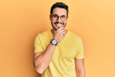 Gündelik giysiler ve gözlük takan genç İspanyol adam kameraya kendinden emin bir şekilde bakıyor kollarını kavuşturup, çenesini kaldırarak gülümsüyor. Olumlu düşünmek. 