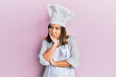 Young beautiful woman wearing professional cook uniform and hat thinking looking tired and bored with depression problems with crossed arms.  clipart