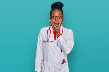 Doktor üniforması ve steteskop giyen genç Afro-Amerikan kadın inançsızlığa, şaşkınlığa ve elleri çenesinde olan şaşkınlık ifadesine hayran kaldı. 
