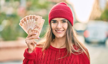 Şehirde elinde Türk lirası banknotları tutan yün şapkalı genç İspanyol kadın..