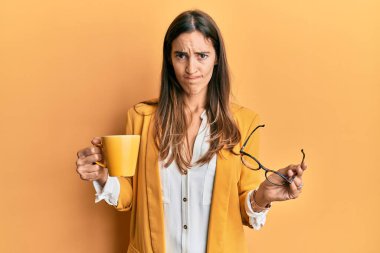 İş tarzı giyinen genç ve güzel bir kadın şüpheci ve gergin bir şekilde bir fincan kahve içiyor sorun yüzünden surat asıyor. negatif kişi. 