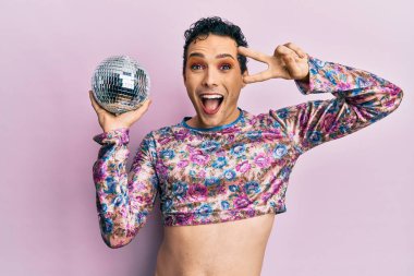 Yakışıklı adam makyaj yapıp parlak disko topunu tutuyor. Çılgınlığı kutluyor ve başarıya hayret ediyor. Gözleri açık, heyecanlı çığlıklar atıyor.. 