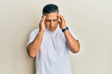 Genç Latin bir adam, stresten dolayı başı ağrıyan günlük beyaz tişörtler giyiyor. migren ağrısı. 