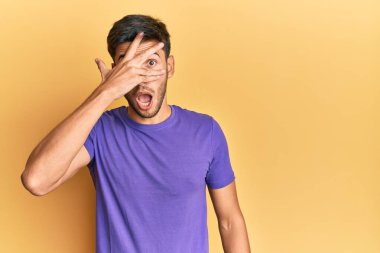 Gündelik kıyafetler giyen genç yakışıklı adam şok içinde yüzünü ve gözlerini eliyle kapatıyor, parmaklarından korkuyla bakıyor. 