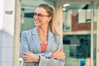 Sarışın iş kadını kollarını kavuşturup şehirde mutlu mesut gülümsüyor..