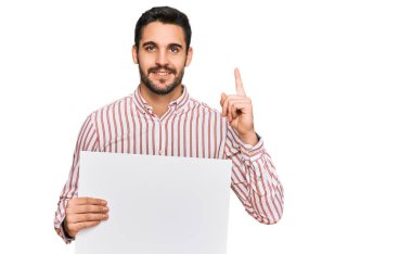 Boş afiş tutan genç İspanyol bir adam bir fikre ya da mutlu yüzle işaret eden bir soruya şaşırdı. 