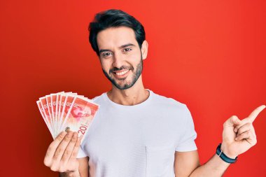 Genç İspanyol adam elinde 20 İsrail şekeri ile gülümsüyor mutlu bir şekilde elini ve parmağını kenarı işaret ediyor. 