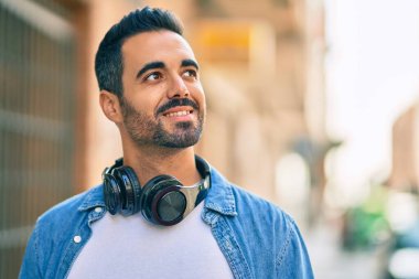 Şehirde kulaklık takarak mutlu gülümseyen genç İspanyol adam..