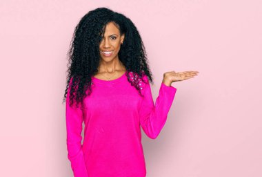 Orta yaşlı Afro-Amerikalı kadın günlük kıyafetler giyiyor neşeli bir şekilde gülümsüyor ve avuç içi kameraya bakıyor.. 