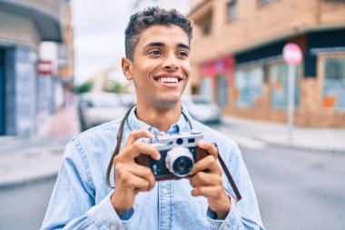 Genç Latin turist mutlu bir şekilde gülümsüyor. Şehirde eski model kamera kullanıyor..