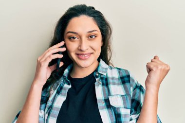 Ortadoğulu güzel bir kadın akıllı telefonda konuşuyor gururla bağırıyor, zaferi kutluyor ve başarıyı kollarını kaldırarak kutluyor. 