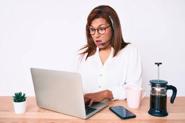 Orta yaşlı esmer, ofiste çalışan, operatör kulaklığı takan, ağzı açık, korkmuş, ağzı açık, imansız bir kadın. 