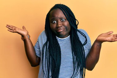 Örgülü, sıradan kıyafetler giyen, kolları açık ve kafası karışık genç siyahi bir kadın. Hiç bir fikrim yok.. 