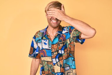 Yazlık tişört giyen, gülümseyen ve gülümseyen genç sarışın adam şaşırtmak için gözlerini kapatıyor. kör kavram. 