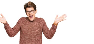 Yakışıklı beyaz adam, günlük süveter ve gözlük takıyor zaferi kutluyor, gülümsüyor ve ellerini kaldırarak kazanan yüz ifadesi sergiliyor. 