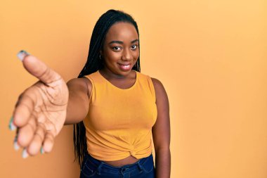 Genç Afrikalı Amerikalı kadın günlük kıyafetler giyip gülümseyerek dostça tokalaşıyor ve hoş geldin diyor. başarılı iş. 