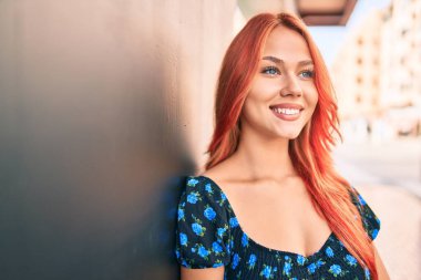 Genç kızıl saçlı kız gülümsüyor Mutlu bir şekilde yürüyor şehrin caddesinde.