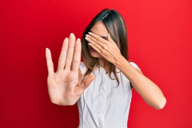 Genç esmer kadın gündelik kıyafetler ve gözlük takıyor. Gözleri ellerle örtüyor ve üzgün ve korku ifadeleriyle jestleri durduruyor. utangaç ve olumsuz kavram. 