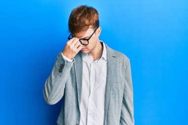 Zarif kıyafetler giyen, gözlüklü, burnu ve gözleri ovuşturmaktan yorgun düşmüş, yorgun ve başı ağrıyan beyaz bir genç. Stres ve hüsran kavramı. 