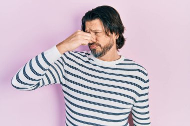 Orta yaşlı, günlük kıyafetler giyen, pis ve iğrenç bir koku alan, nefesini burnunda tutan beyaz bir adam. Kötü kokuyor. 