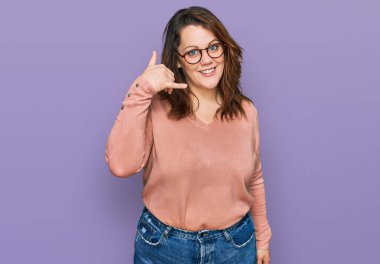 Genç ve cüsseli bir kadın günlük kıyafetler ve gözlük takıyor gülümsüyor telefonla el ve parmaklarıyla jest yapıyor telefonda konuşuyor gibi. iletişim kavramları. 