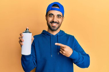 Süveter giyen genç İspanyol adam elinde grafiti spreyi tutarken mutlu bir şekilde elini ve parmağını gösterdi. 