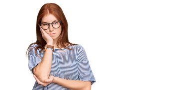 Gündelik giysiler ve gözlük takan genç bir kadın kollarını kavuşturarak depresyondan sıkılmış ve yorgun göründüğünü düşünüyor.. 