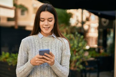 Genç İspanyol kız şehirde akıllı telefon kullanarak mutlu bir şekilde gülümsüyor..