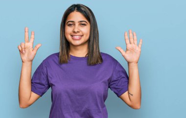 Latin asıllı genç bir kız günlük mor tişört giyer ve 8 numaralı parmaklarını göstererek gülümseyerek mutlu ve kendinden emin. 