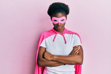 Young african american girl wearing superhero mask and cape costume skeptic and nervous, disapproving expression on face with crossed arms. negative person. 
