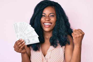 Dolarları tutan güzel Afrikalı kadın gururla bağırıyor, zaferi kutluyor ve başarıyı kollarını kaldırarak kutluyor. 